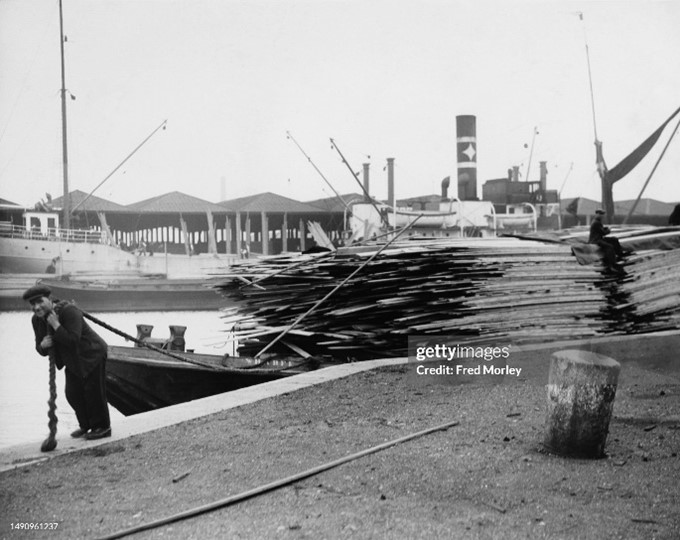 Surrey Commercial Docks, a dockworker hauling a barge loaded with lengths of timber, c1935.  X..jpg
