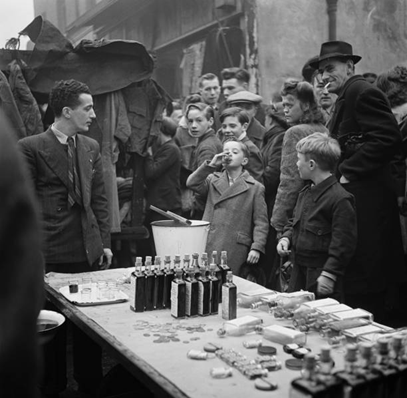 East Street Market c1947. A boy tastes a sample of a coloured liquid on sale at a medicine stall..png